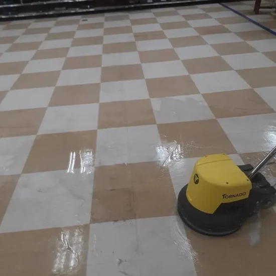 A yellow cleaning machine operates on a checkered floor, effectively removing dirt and debris.